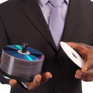 This is an image of a business man holding a stack of DVDs/CDs. This can be used to represent ""Data Service"" , ""Software Backup"", ""Information Technologies"", ""DVD and CD sales"" etc..